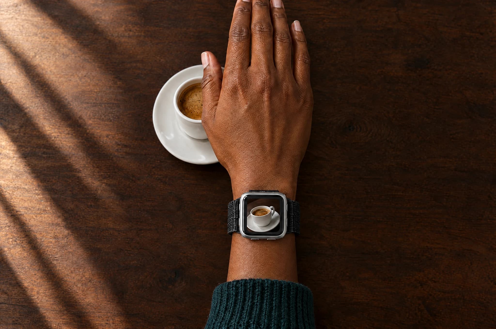 A right hand hovering over coffee, with an oblique band-camera view on the watch screen